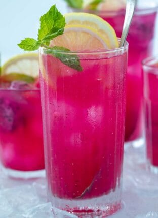 Four glasses filled with bright pink mango dragonfruit refresher. Glasses are garnished with lemon slices and mint leaves.
