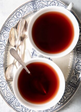 Two white cups of elderberry tea sit on a blue and white oval platter