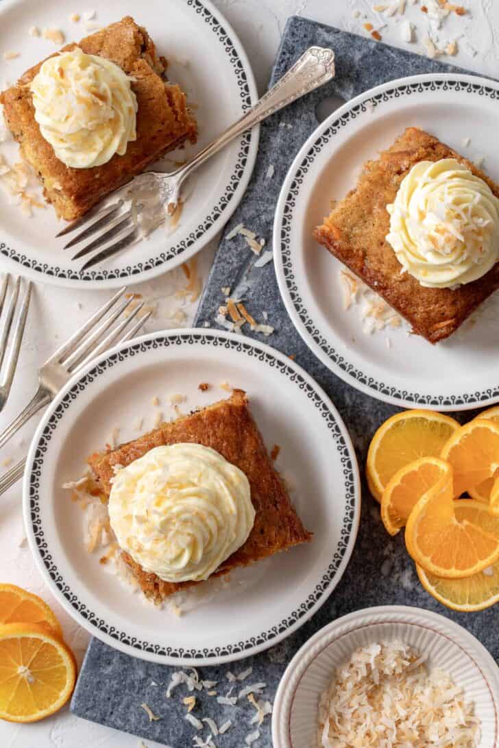 Three white plates with a piece of carrot sheet cake topped with orange cream cheese frosting.