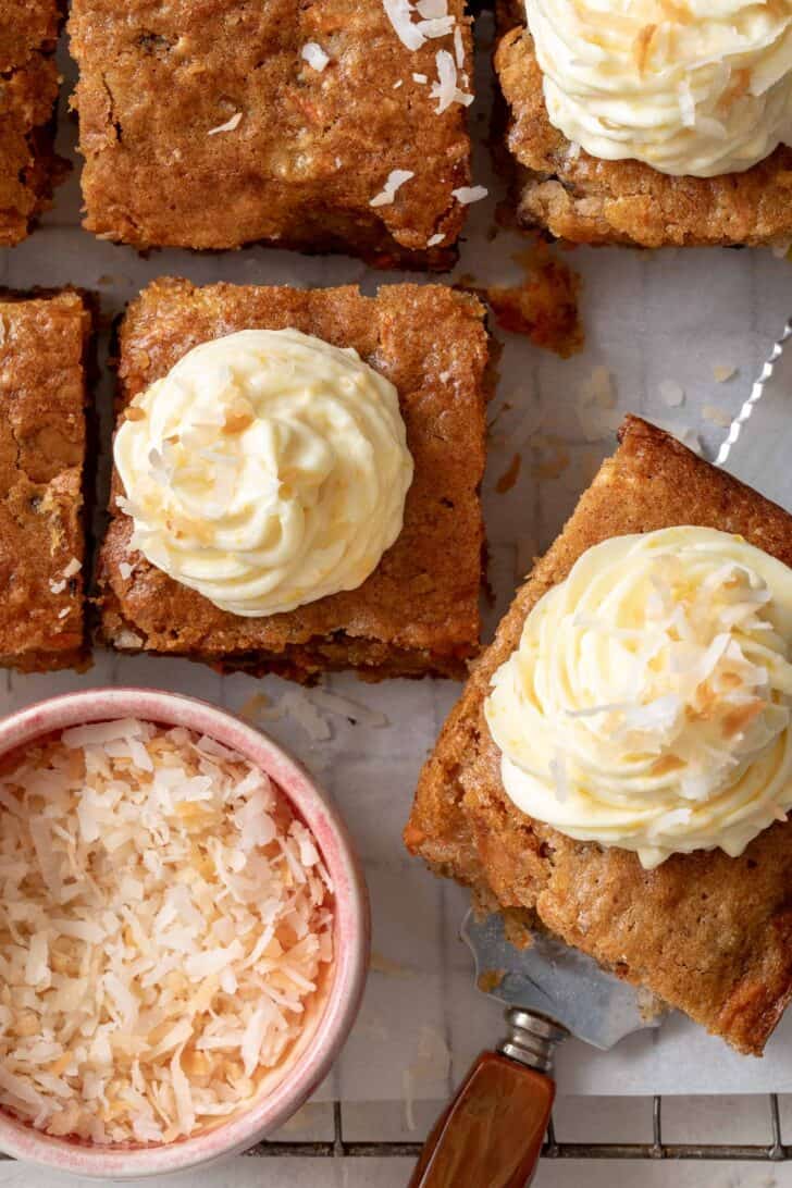 Six slices of carrot sheet cake with orange cream cheese piped on top.