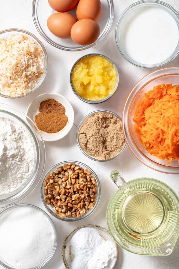 Clear glass measuring bowls filled with flour, sugar, eggs, coconut, pineapple, oil to make a dessert.