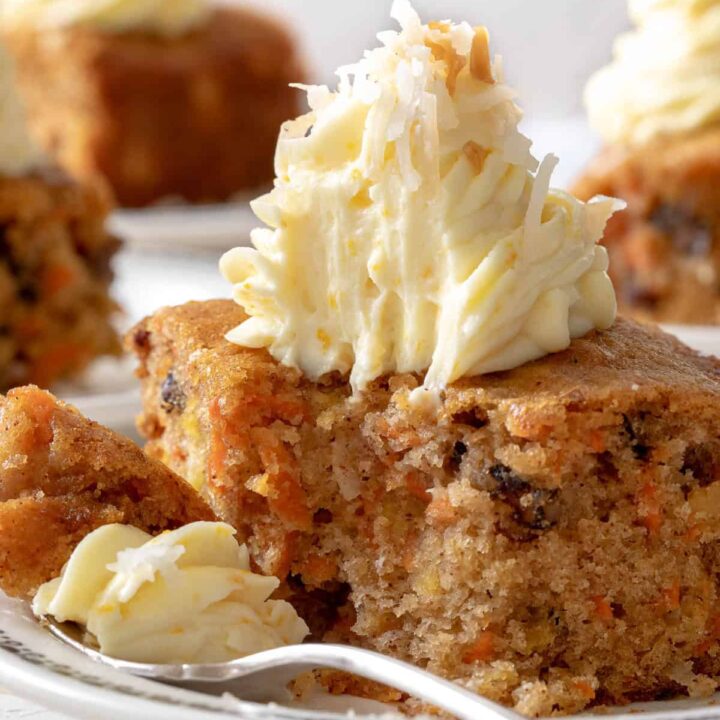 Three white plates with pieces of carrot cake on them. A fork rests on one of the plates.