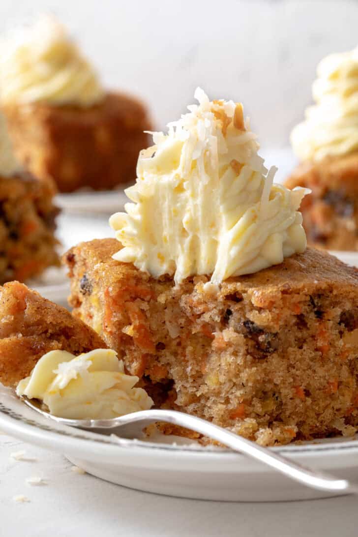 Three white plates with pieces of carrot cake on them. A fork rests on one of the plates.