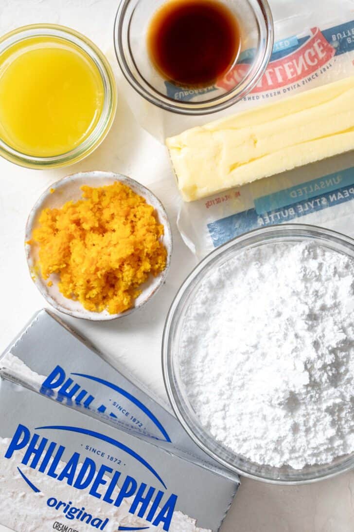 Two sticks of cream cheese next to a stick of butter and a small glass bowl filled with powdered sugar.