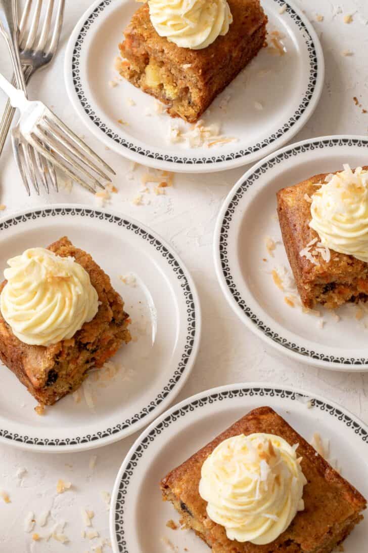 Four white dessert plates with pieces of carrot sheet cake topped with orange cream cheese frosting.