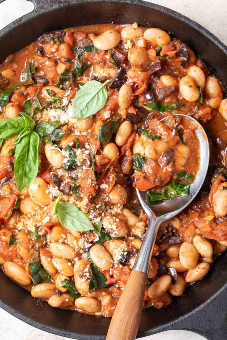 A cast iron skillet filled with Italian Butter Beans. A serving spoon with a wooden handle rests in the skillet.
