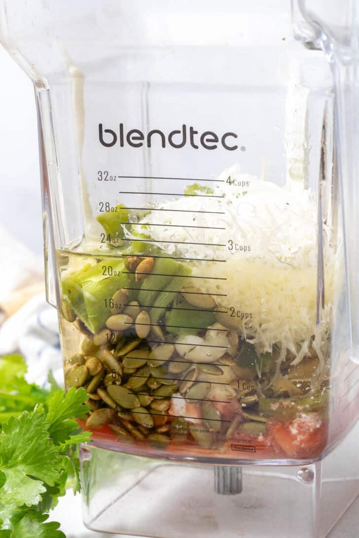 A blendtec blender container filled with cheese, peppers, pepitas, mayonnaise, sour cream and red wine vinegar.
