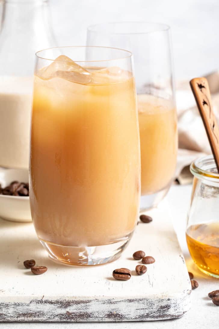 Two clear glasses filled with Iced Coffee Flavored Water. A small jar filled with honey sits next to the glasses.