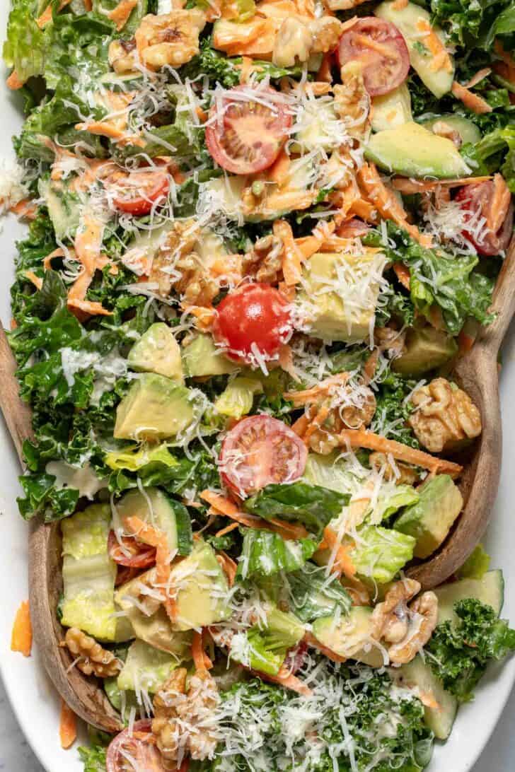 A white platter filled with mixed greens tossed with chopped avocado, walnuts, grated carrot, and cherry tomatoes.
