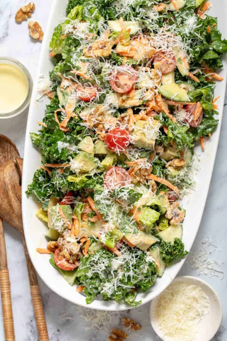 A white platter filled with lemony kale salad. Wooden salad servers rest next to the platter.