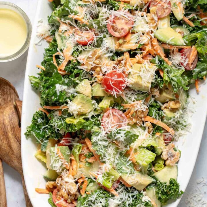 A white platter filled with Lemon Kale Salad. Wooden salad servers rest next to the platter.