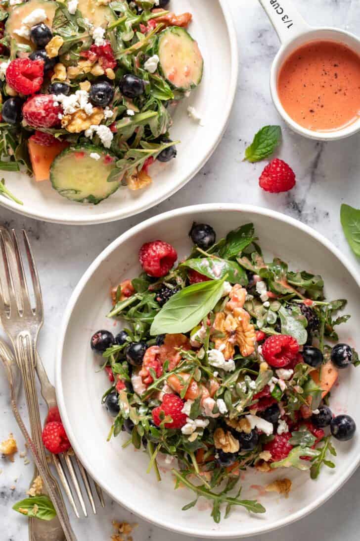 Two white plates filled with Arugula Berry Salad. Three forks sit next to the plate.