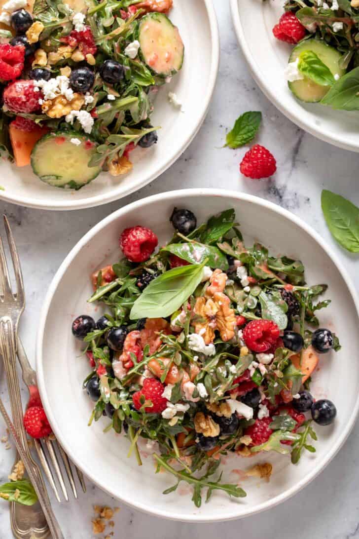 Three white plates filled with greens and fruit. Three forks sit next to the plates.