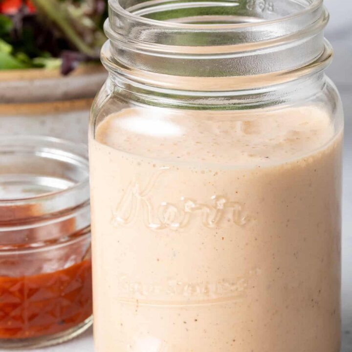 A clear mason jar filled with BBQ Ranch Dressing. A tan bowl filled with salad sits next to the jar.