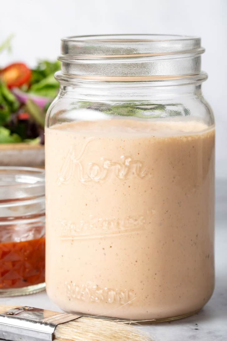 A mason jar filled with an orange creamy sauce. A bowl of mixed greens sits next to the bowl.