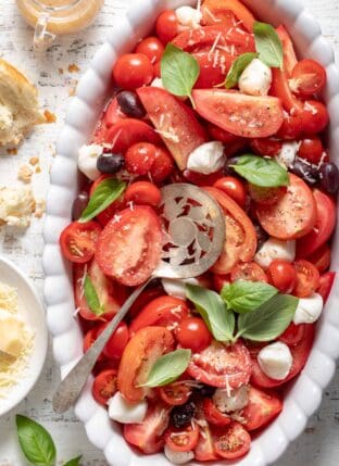 A white oval platter filled with Caprese Salad. A tomato server rests on the platter.