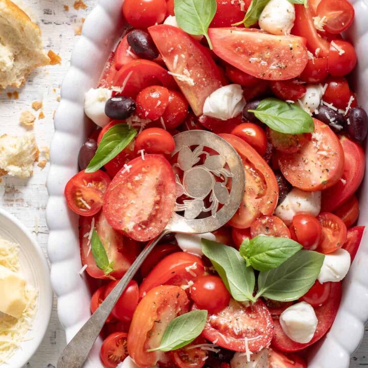 A white oval platter filled with Caprese Salad. A tomato server rests on the platter.