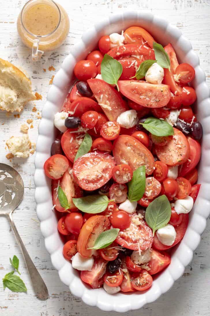 A white oval platter filled with tomato Caprese salad. A tomato server sits next to the platter.