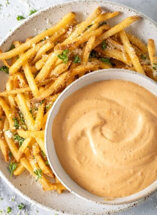 A bowl filled with Chipotle Aioli sits on a plate filled with French fries.
