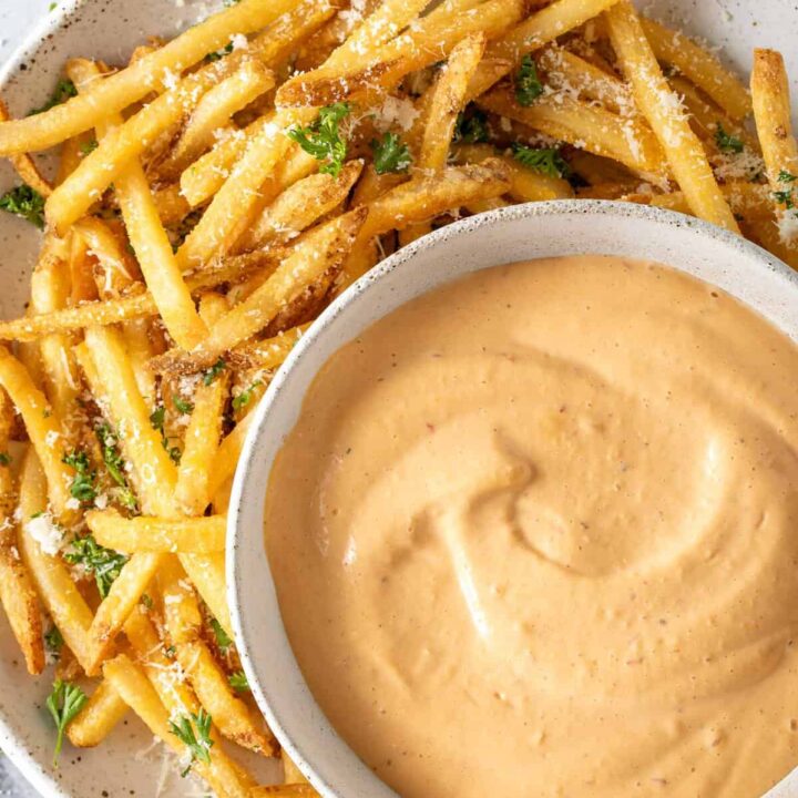 A bowl filled with Chipotle Aioli sits on a plate filled with French fries.