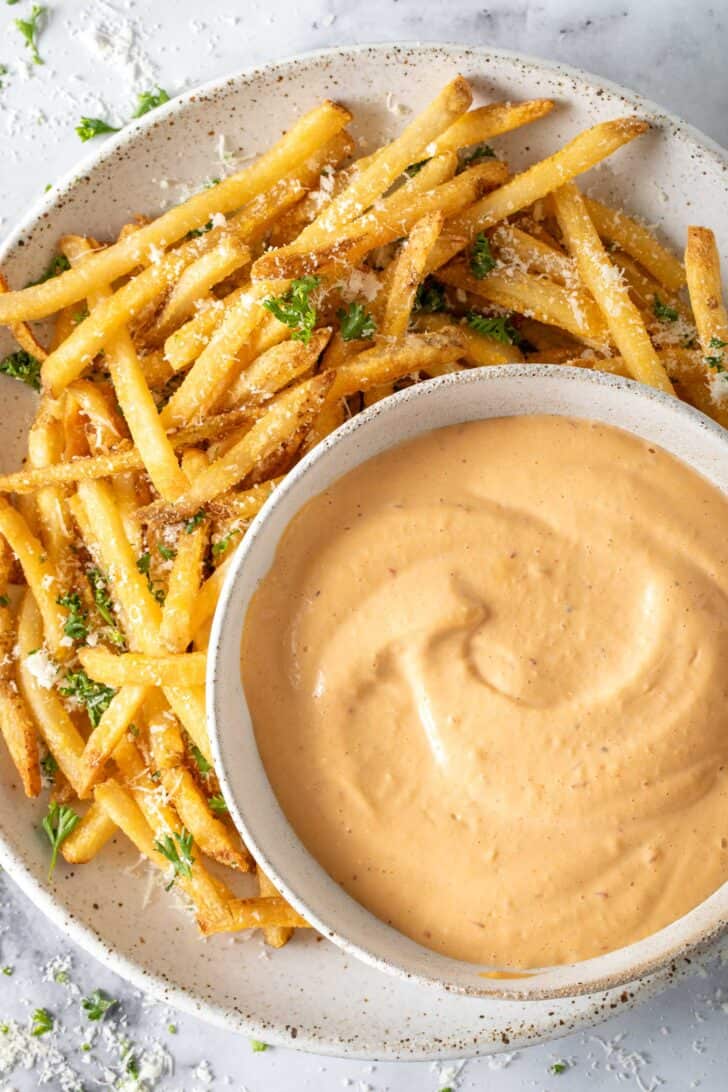 A bowl filled with Chipotle Aioli sits on a plate filled with French fries.