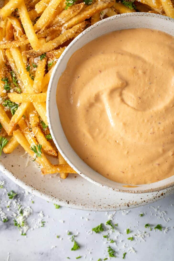 A bowl filled with Chipotle Aioli sits on a plate filled with French fries.