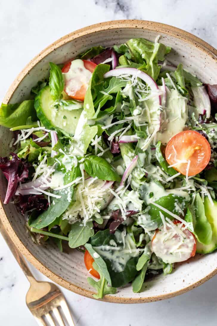 A tan colored bowl filled with mixed greens and sliced cherry tomatoes.