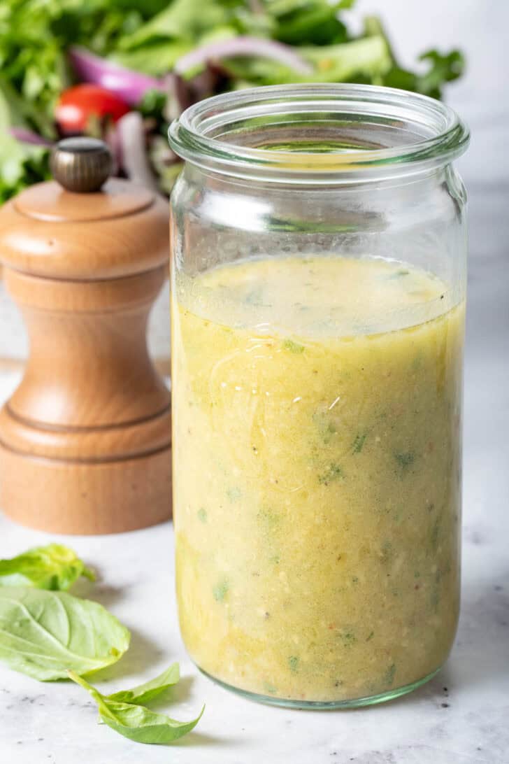 A clear mason jar filled with a citrus blend to toss with mixed greens. A pepper mill sits next to the jar.