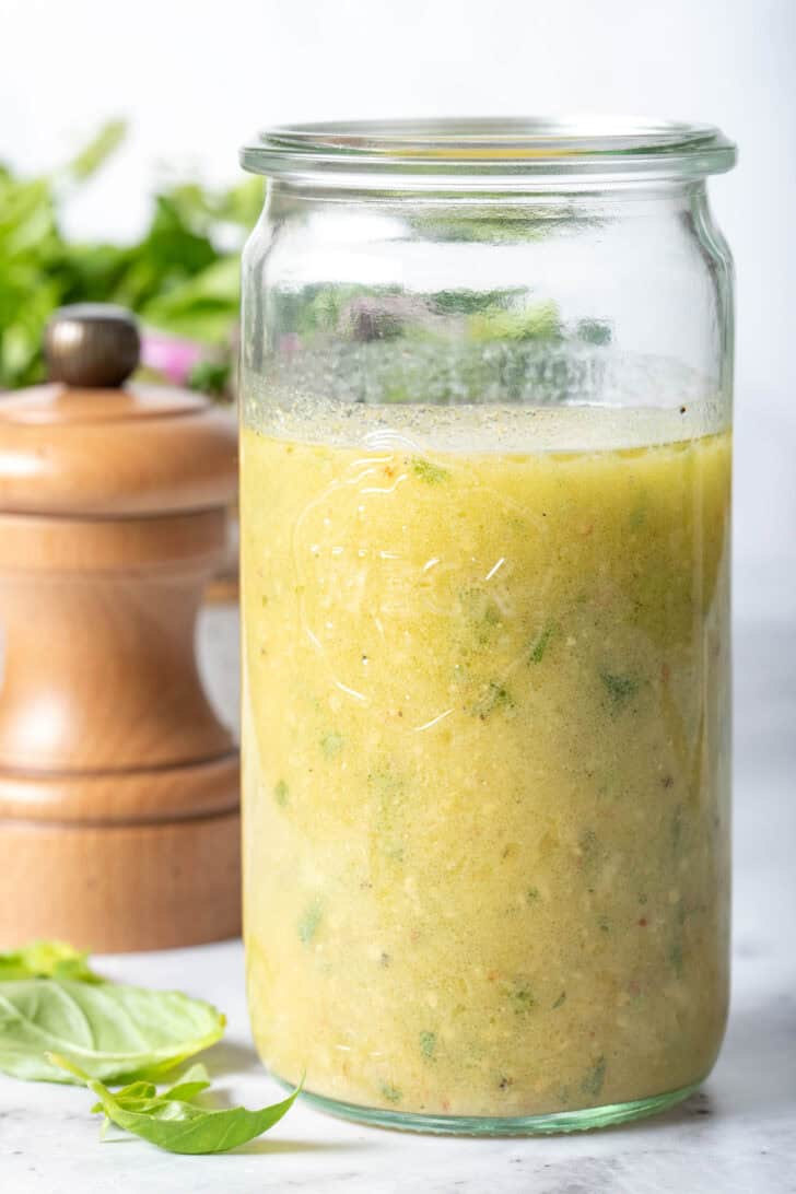 A clear glass mason jar filled with Fresh Basil Dressing. A wooden pepper mill sits next to the jar.