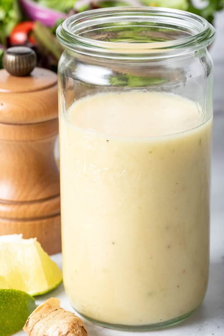 A clear glass mason jar filled with Lime Ginger Salad Dressing. A wooden pepper mill sits next to the jar.