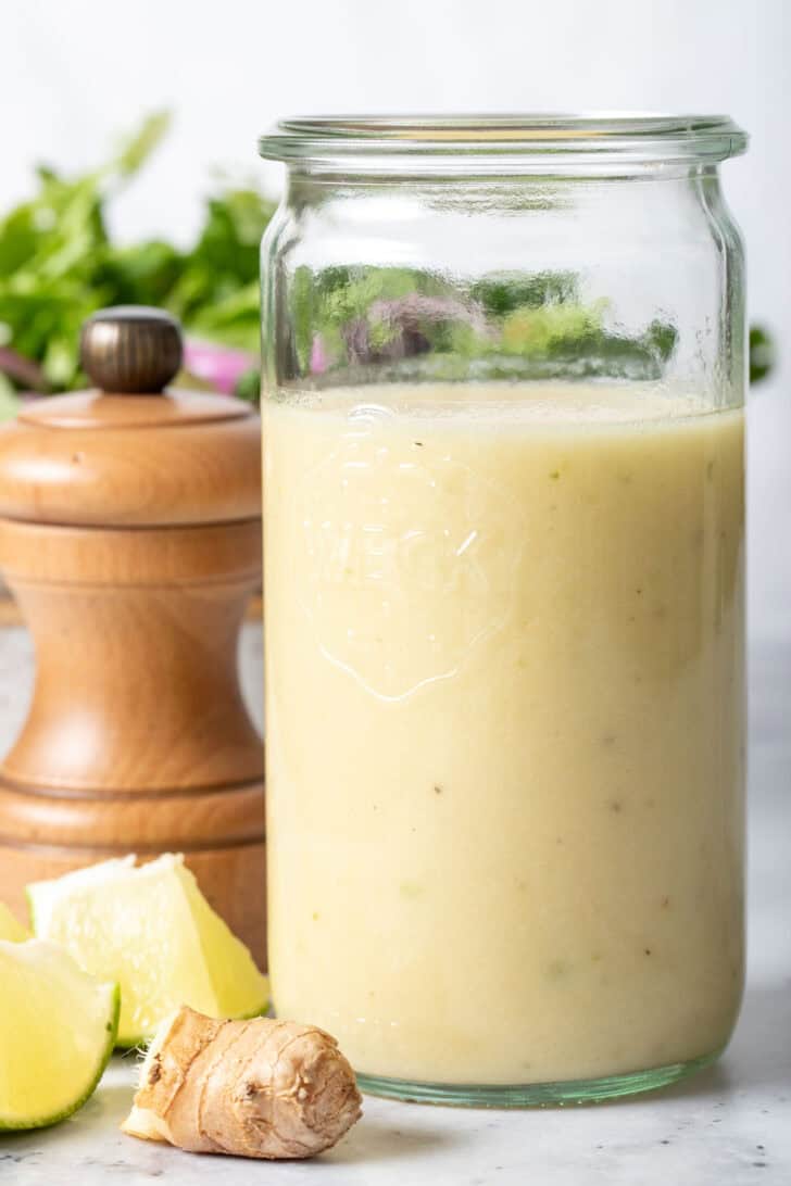 A clear glass mason jar filled with Lime Ginger Salad Dressing. A wooden pepper mill sits next to the jar.