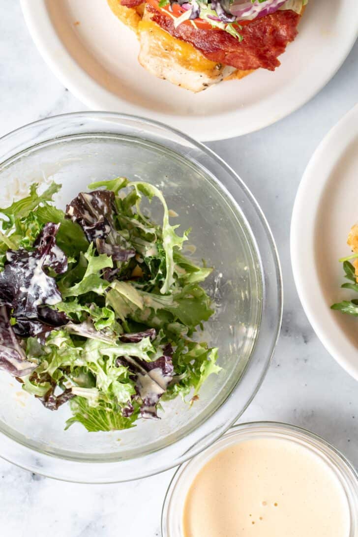 A clear glass bowl filled with salad greens tossed in a creamy dressing.