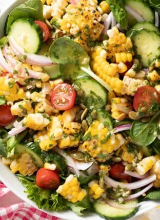 A white bowl filled with Summer Corn Salad made with grilled corn, tomato, cucumber, red onion, pepitas and cilantro lime vinaigrette.