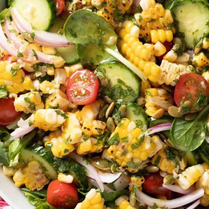 A white bowl filled with Summer Corn Salad made with grilled corn, tomato, cucumber, red onion, pepitas and cilantro lime vinaigrette.