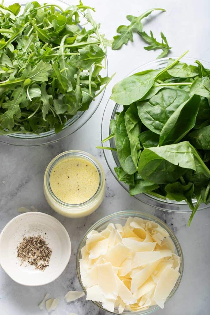 Clear glass mixing bowls filled with mixed greens and a dressing.