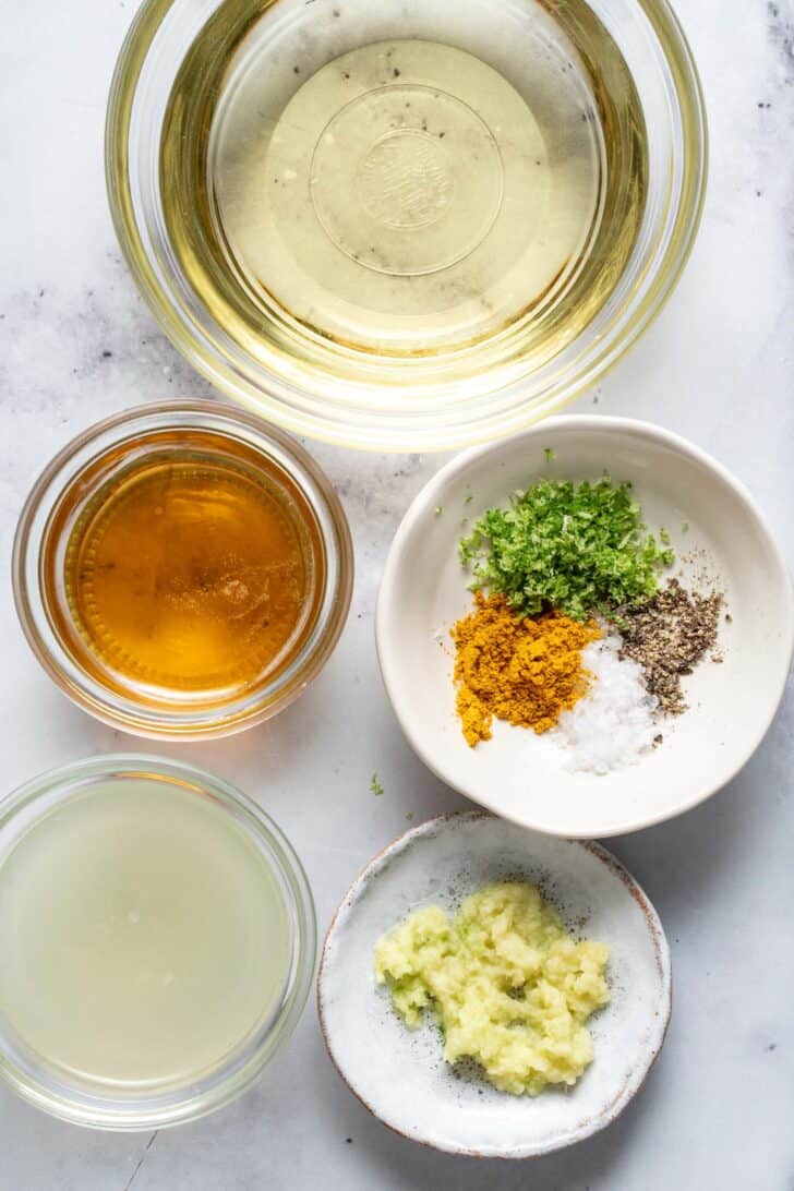 Clear glass bowls filled with citrus juice, olive oil, honey and seasonings.