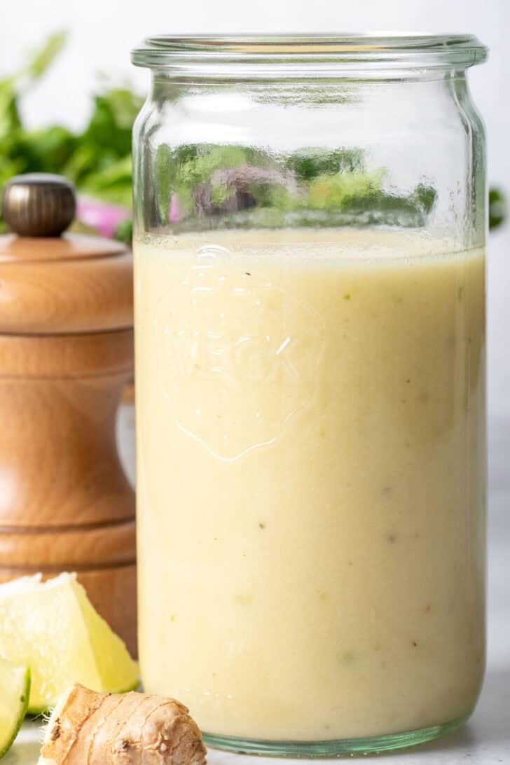 A clear glass mason jar filled with salad dressing. A wooden pepper mill sits next to the jar.