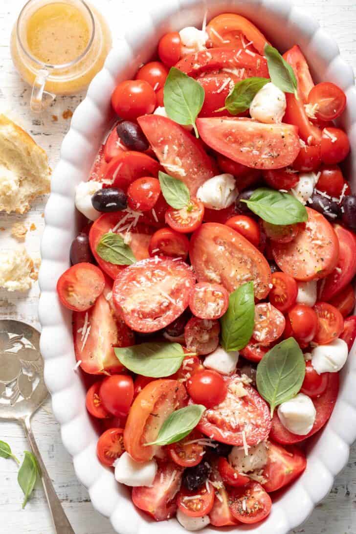 A white oval platter filled with a tomato mozzarella basil salad.