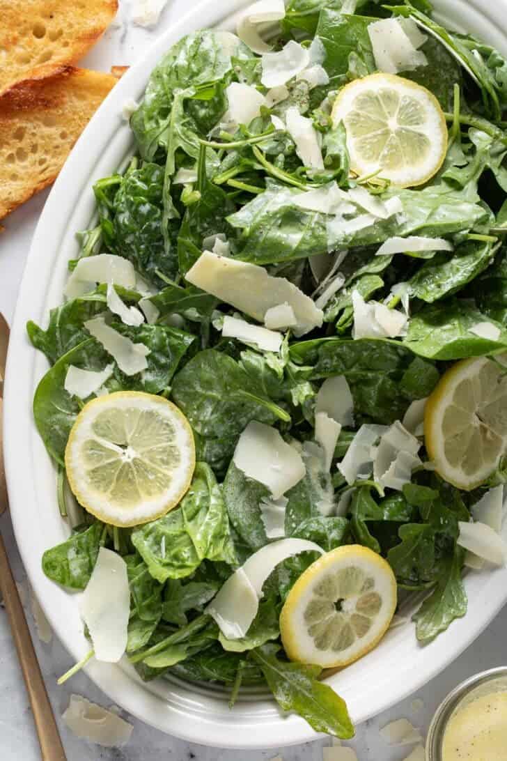 A white oval platter filled with a simple Arugula Salad.