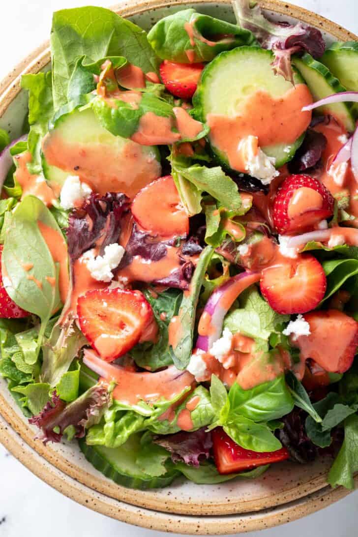 A tan colored bowl filled with mixed greens and fruit tossed with pink dressing.