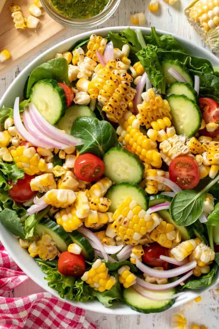 A white bowl filled with mixed greens and vegetables. A red and white checked napkin sits next to the bowl.