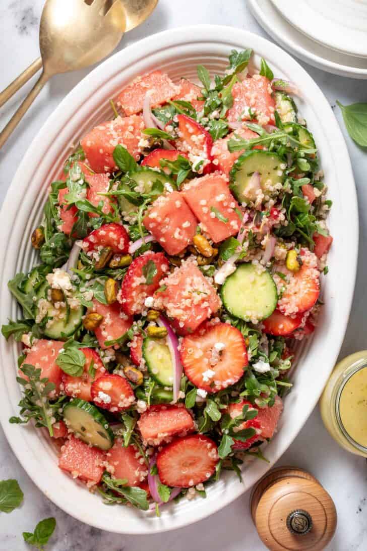 A white oval platter filled with watermelon arugula salad with feta cheese.