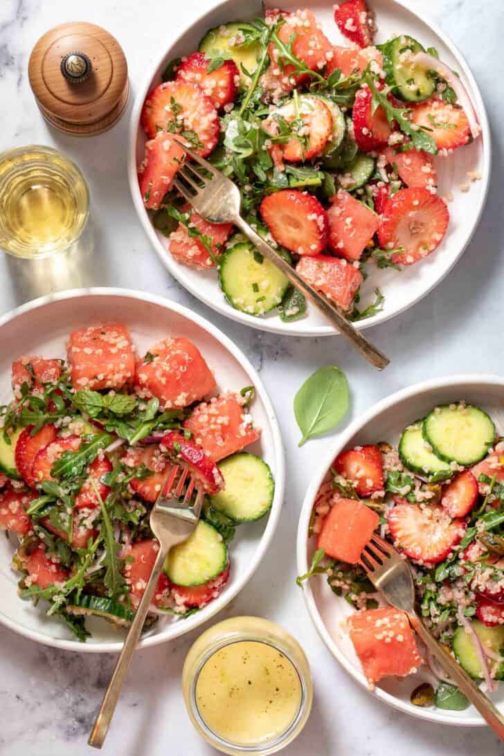 Three white plates filled with greens and chopped fruit. Gold colored forks rest on the plates.