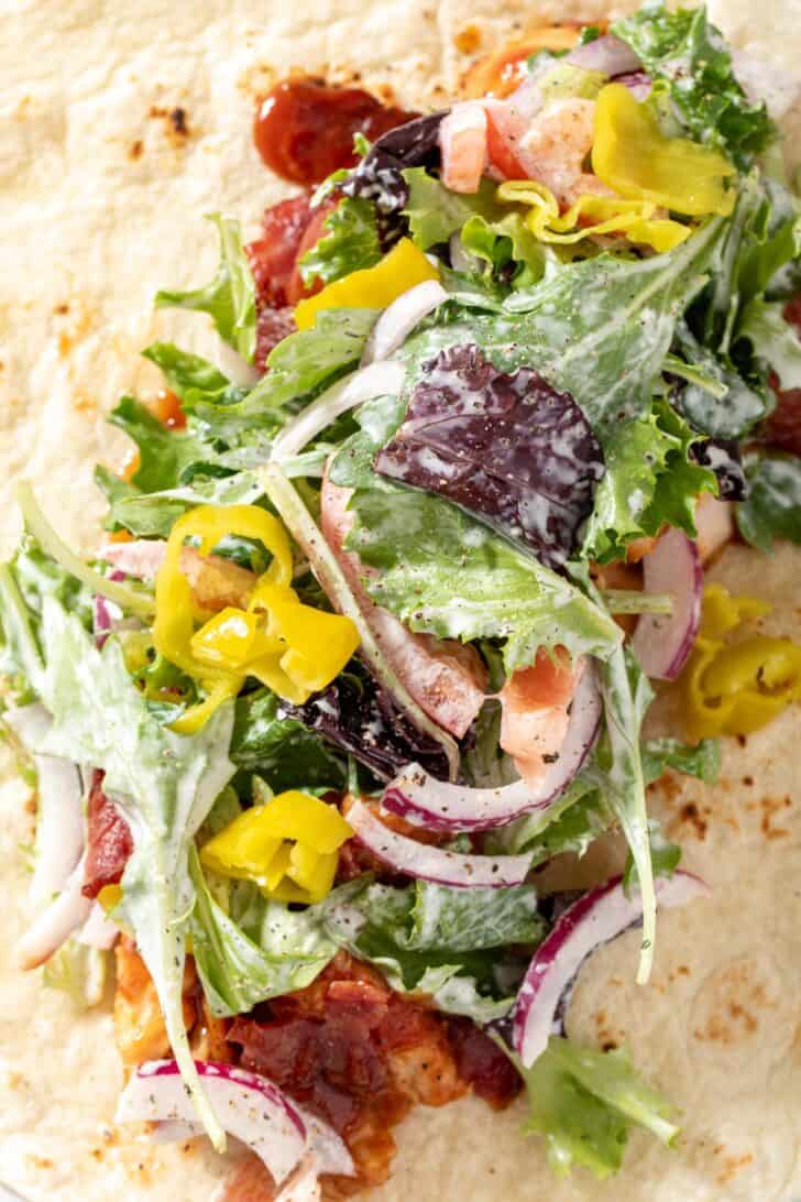 A flour tortilla with mixed greens on top of cooked poultry with barbecue sauce.