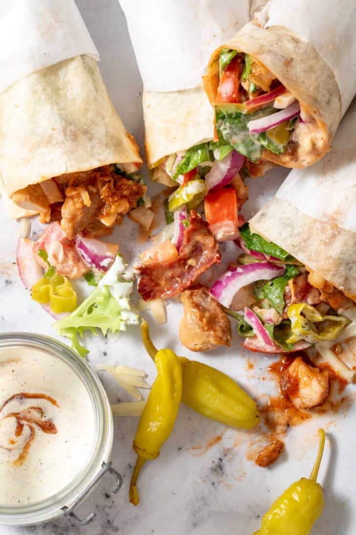 Four BBQ Chicken Wraps laying on a countertop with potato chips scattered next to them.