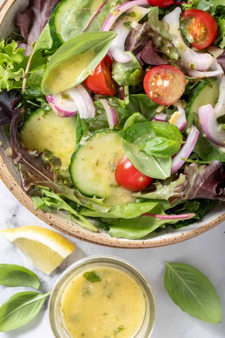 A wooden bowl filled with mixed greens, cucumber slices, onion slices and cherry tomatoes.