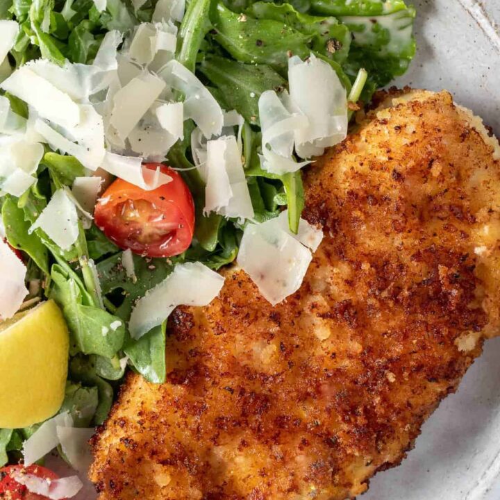 A white plate filled with arugula salad and Easy Parmesan Crusted Chicken cutlets.