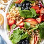 A white platter filled with Strawberry Spinach Quinoa Salad made with quinoa, spinach, strawberries, blueberries and apple slices.