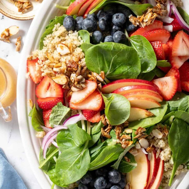 A white platter filled with Strawberry Spinach Quinoa Salad made with quinoa, spinach, strawberries, blueberries and apple slices.