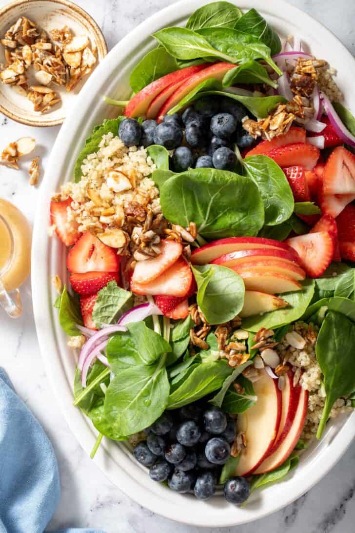 A white platter filled with Strawberry Spinach Salad made with spinach, strawberries, blueberries and sliced apple.